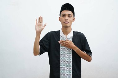 Müslüman Asyalı bir adam, mutlu bir yüz ifadesiyle kameraya bakarken, diğerlerini selamlamak için elini sallıyor.