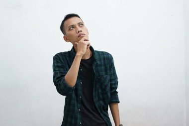 Düşünen genç Asyalı bir adamın portresi günlük giysiler giymiş beyaz arka plandan izole edilmiş bir şekilde yukarı bakıyor.