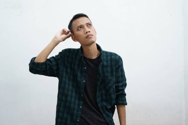 Düşünen genç Asyalı bir adamın portresi günlük giysiler giymiş beyaz arka plandan izole edilmiş bir şekilde yukarı bakıyor.