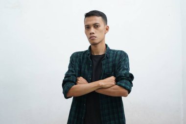 Koyu yeşil giyimli genç Asyalı bir adamın portresi. Şüpheli alaycı bir ifadeyle kameraya bakıyor. Beyaz arka planda kollarını göğsüne kavuşturmuş.