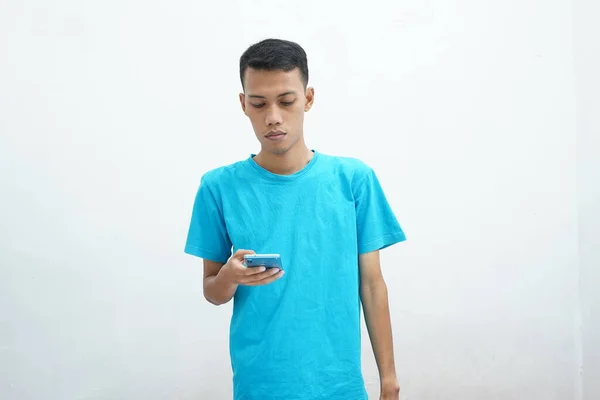 Young Asian Man Wearing Blue Shirt Looks Attentively Smartphone Screen — стоковое фото