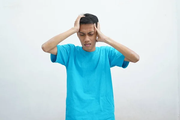 亚洲年轻人的画像 身穿蓝色T恤 严重头痛 手指紧贴太阳穴 用无助的面部表情减轻疼痛 — 图库照片