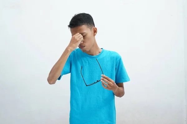 年轻的亚洲人穿着不健康的蓝色T恤 戴着眼镜 揉着眼睛 视力模糊 眼睛干瘪 被白色背景隔离 健康问题概念 — 图库照片