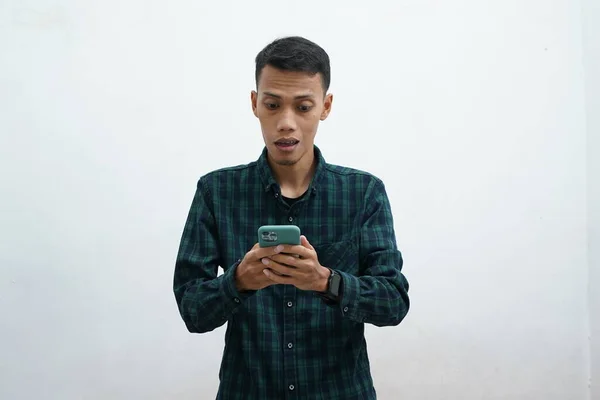 亚洲人穿着深绿色的衬衫 用智能手机 他看着电话 看上去很惊讶 白人背景 — 图库照片