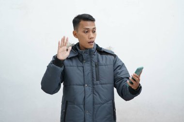 İzole edilmiş beyaz arka planda kışlık ceket giyen Asyalı bir adam. Akıllı telefon kullanarak video araması yapmaktan mutlu.