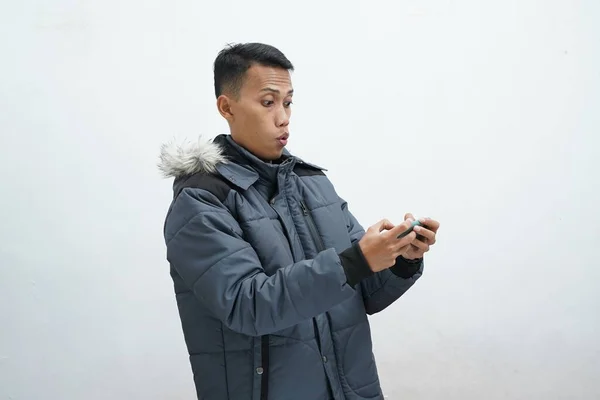 亚洲人穿着冬季夹克 背景是孤立的白色 他看着电话 看起来真的很惊讶 — 图库照片