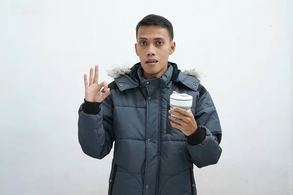 亚洲人穿着冬季夹克 拿着外卖咖啡 背景是孤立的白色背景 感到惊讶 并显示出确定的迹象 — 图库照片