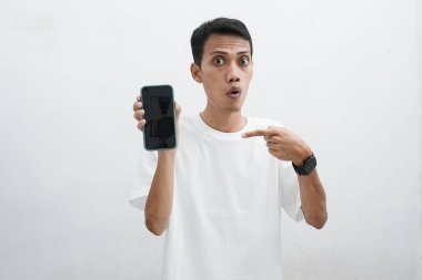 Akıllı telefon kullanan Asyalı bir adam. Telefona bakıyor ve çok şaşırmış görünüyor. Beyaz arka planda beyaz bir tişört giyiyor..
