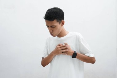 Beyaz tişört giyen genç Asyalı adam beyaz arka planda göğsünde ağrı hissediyor.