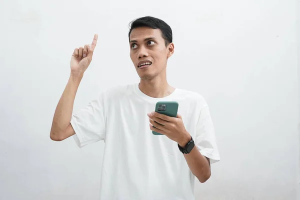 Ázsiai Fiatal Férfi Gazdaság Smartphone Felnézett Döntött Gondolkodás Szkeptikus Kifejezés — Stock Fotó