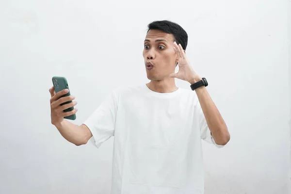 身穿白色T恤的亚洲人似乎对自己从智能手机中得到的好消息感到惊讶 男人用锐利的目光看着智能手机 表现出震惊的姿态 — 图库照片