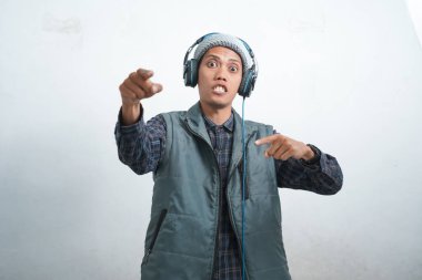 Asian young man wearing navy blue vest and beanie wearing headphones, isolated on white background showing expression listening to rock music.
