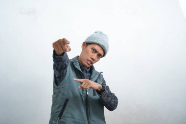 Asian young man wearing navy blue vest and beanie, isolated on white background smiling and looking cool pointing at camera.