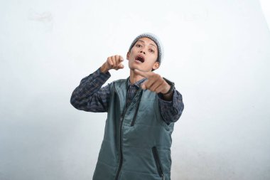 Asian young man wearing navy blue vest and beanie, isolated on white background smiling and looking cool pointing at camera.