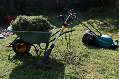 Mevsimlik bahçe işleri. Çimenli yeşil el arabası, arka bahçede elektrikli çim biçme makinesi.. 