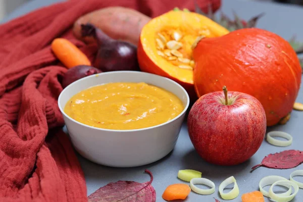 Squash soup with coconut milk, carrot, apple and spices. Top view photo of tasty pumpkin soup on red kitchen towel. Colors of Autumn on a table.