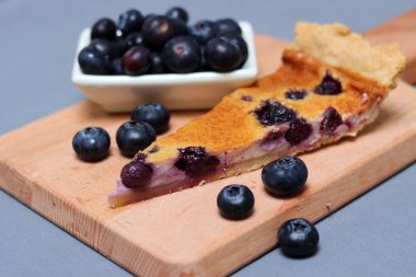 Tahta kesme tahtasının üzerinde yabanmersinli tart dilimi. Masadaki yaban mersinli pasta. Ev yapımı tatlı yakın plan fotoğraf. Sağlıklı beslenme konsepti. Kopyalama alanı olan gri arkaplan. 