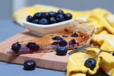 Cheesecake dilimi, yabanmersini, ahşap kesim tahtası, çatal ve masa üzerinde sarı mutfak havlusu. Yabanmersinli turtanın yakın çekimini yap. Geleneksel Fin makbuzu. 