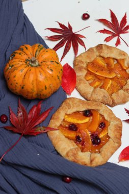 Balkabaklı börekler, kırmızı akçaağaç yaprakları ve masa üzerindeki dekoratif kabak. Sonbahar yemeği. Mevsimlik sebzeler ve balkabağı turtasıyla. 