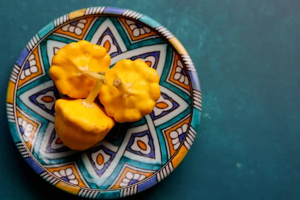 Patty pan squash on decorative ceramic plate. Sill life with vegetables. Beautiful yellow patty pan squashes close up photo.  Textured background with copy space.