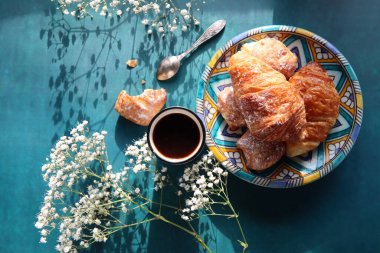 Günaydın! Günaydın! Masada sade kahve ve kruvasan. Hamur işleri ve çiçeklerle dolu güneşli bir resim. Yemek, natürmort. 