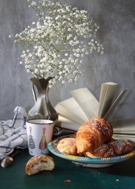 Günaydın! Günaydın! Masada sade kahve ve kruvasan. Hamur işleri ve çiçeklerle dolu güneşli bir resim. Yemek, natürmort. 