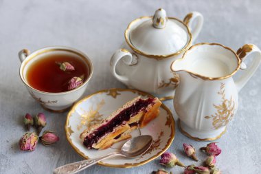 Bir fincan çay, bir sürahi süt, vişneli turta, küçük gül çiçekleri ile sakin bir hayat. Masadaki beyaz antika sofra takımı. Güzel kahvaltı. Yakın plan fotoğraf.. 
