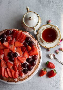 Masanın üzerinde retro masa takımı var. Bir fincan çay, süt sürahisi, taze böğürtlen ve çilekli kek. Kopyalama alanı olan desenli arkaplan. 