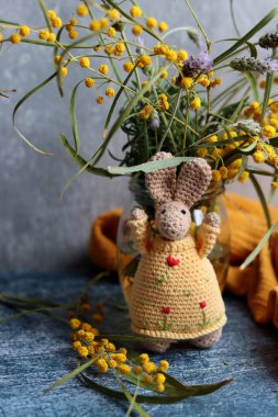 Örgü ören Paskalya tavşanı gri arka planda. Masada güzel bir bahar buketi mimoza ve lavanta çiçekleri. Hobiler ve boş zaman kavramı.  