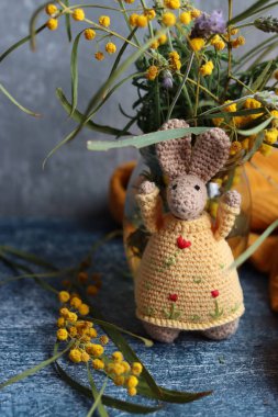 Örgü ören Paskalya tavşanı gri arka planda. Masada güzel bir bahar buketi mimoza ve lavanta çiçekleri. Hobiler ve boş zaman kavramı.  
