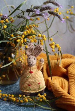 Örgü ören Paskalya tavşanı gri arka planda. Masada güzel bir bahar buketi mimoza ve lavanta çiçekleri. Hobiler ve boş zaman kavramı.  