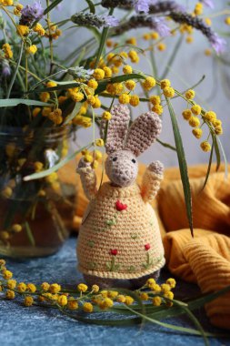 Örgü ören Paskalya tavşanı gri arka planda. Masada güzel bir bahar buketi mimoza ve lavanta çiçekleri. Hobiler ve boş zaman kavramı.  