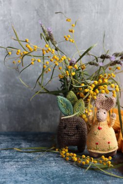 Örgü ören Paskalya tavşanı gri arka planda. Masada güzel bir bahar buketi mimoza ve lavanta çiçekleri. Hobiler ve boş zaman kavramı.  