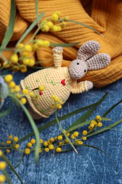 Örgü ören Paskalya tavşanı gri arka planda. Masada güzel bir bahar buketi mimoza ve lavanta çiçekleri. Hobiler ve boş zaman kavramı.  