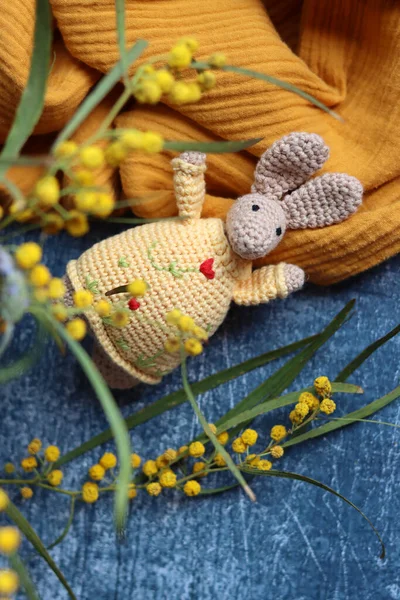 Örgü ören Paskalya tavşanı gri arka planda. Masada güzel bir bahar buketi mimoza ve lavanta çiçekleri. Hobiler ve boş zaman kavramı.  