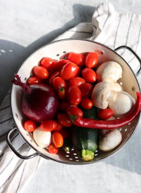 Taze organik sebzeler ve beyaz kevgir. Kırmızı soğan, kiraz domatesleri, şampiyonlar, kırmızı biber ve kabağın yakın plan fotoğrafı.. 