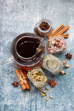 Siyah çayla çaydanlık, güllerle dolu cam kavanozlar, lavanta, karanfil, kakule, anason yıldızları ve tarçınlı çubuklar. Masadaki çay baharatlarının farklı türleri. Kopyalama alanı olan desenli arkaplan. 