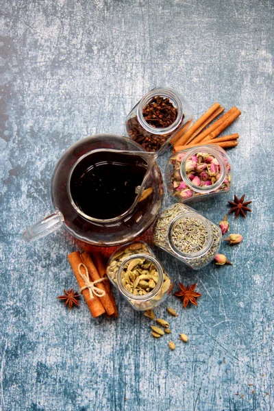 Siyah çayla çaydanlık, güllerle dolu cam kavanozlar, lavanta, karanfil, kakule, anason yıldızları ve tarçınlı çubuklar. Masadaki çay baharatlarının farklı türleri. Kopyalama alanı olan desenli arkaplan. 