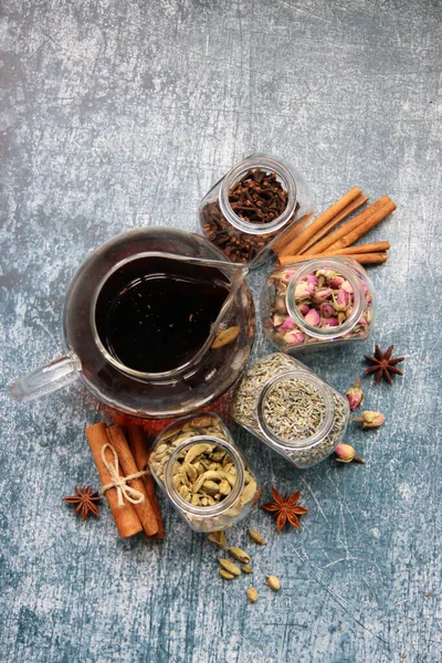 Siyah çayla çaydanlık, güllerle dolu cam kavanozlar, lavanta, karanfil, kakule, anason yıldızları ve tarçınlı çubuklar. Masadaki çay baharatlarının farklı türleri. Kopyalama alanı olan desenli arkaplan. 