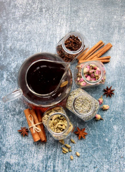 Siyah çayla çaydanlık, güllerle dolu cam kavanozlar, lavanta, karanfil, kakule, anason yıldızları ve tarçınlı çubuklar. Masadaki çay baharatlarının farklı türleri. Kopyalama alanı olan desenli arkaplan. 