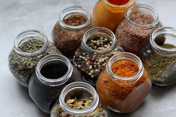 Cam kavanozlardaki çeşitli baharatların fotoğrafını kapat. Kakule, keten tohumu, karışık biber, lavanta, köri ve zerdeçal.. 