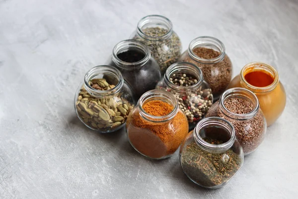 Different types of spices in glass jars. Close up photo of food flavors. Cardamom, turmeric, lavender, curry, pepper and flax seeds.