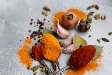 Baharatlı kaşıklar yakın çekim fotoğrafı. Zerdeçal, paprika tozu, bezelye, sarımsak, biber, masada defne yaprağı. Aromatik baharat ve bitkilerin renkli bir resmi. 
