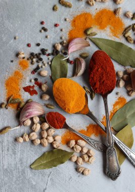 Baharatlı kaşıklar yakın çekim fotoğrafı. Zerdeçal, paprika tozu, bezelye, sarımsak, biber, masada defne yaprağı. Aromatik baharat ve bitkilerin renkli bir resmi. 