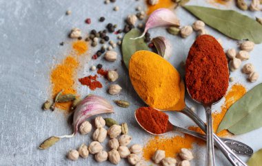 Baharatlı kaşıklar yakın çekim fotoğrafı. Zerdeçal, paprika tozu, bezelye, sarımsak, biber, masada defne yaprağı. Aromatik baharat ve bitkilerin renkli bir resmi. 