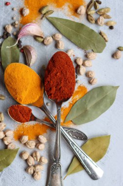 Gümüş kaşıklar, zerdeçal, paprika tozu, defne yaprağı ve biberli hayat. Hint baharatlarının canlı renkleri. Aromatik baharatlar ve bitkiler masada. Yiyecek çeşnileri dokusu yakın.. 
