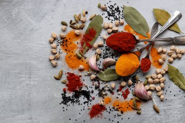 Baharatlı kaşıklar yakın çekim fotoğrafı. Zerdeçal, paprika tozu, bezelye, sarımsak, biber, masada defne yaprağı. Aromatik baharat ve bitkilerin renkli bir resmi. 