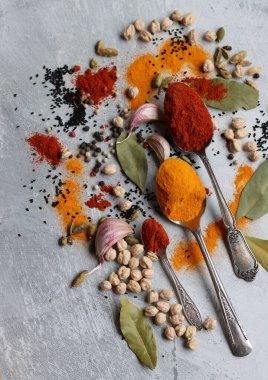 Baharatlı kaşıklar yakın çekim fotoğrafı. Zerdeçal, paprika tozu, bezelye, sarımsak, biber, masada defne yaprağı. Aromatik baharat ve bitkilerin renkli bir resmi. 