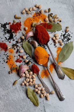 Baharatlı kaşıklar yakın çekim fotoğrafı. Zerdeçal, paprika tozu, bezelye, sarımsak, biber, masada defne yaprağı. Aromatik baharat ve bitkilerin renkli bir resmi. 