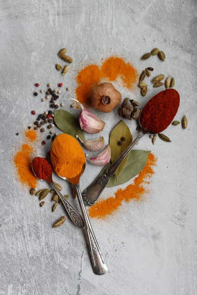 Hint baharatlı gümüş kaşıklar. Zerdeçal, kakule, paprika tozu, defne yaprağı ve açık gri zemin üzerinde fotokopi alanı olan sarımsak.. 